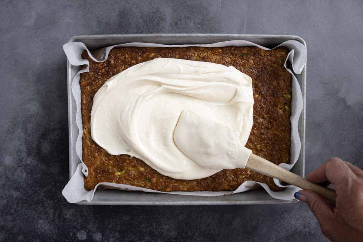 spreading cream cheese frosting on a cake