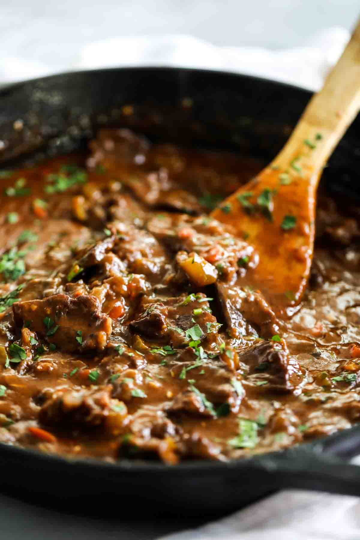 beef tips and gravy in a skillet with a wooden spoon