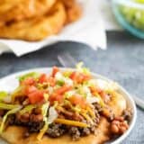 Navajo taco topped with meat and beans with fry bread in the background