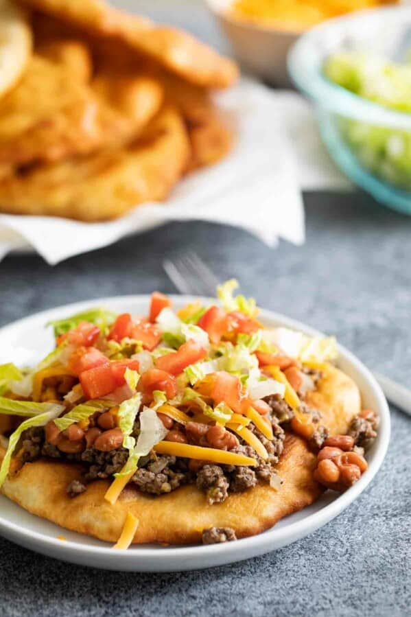 Navajo taco topped with meat and beans with fry bread in the background