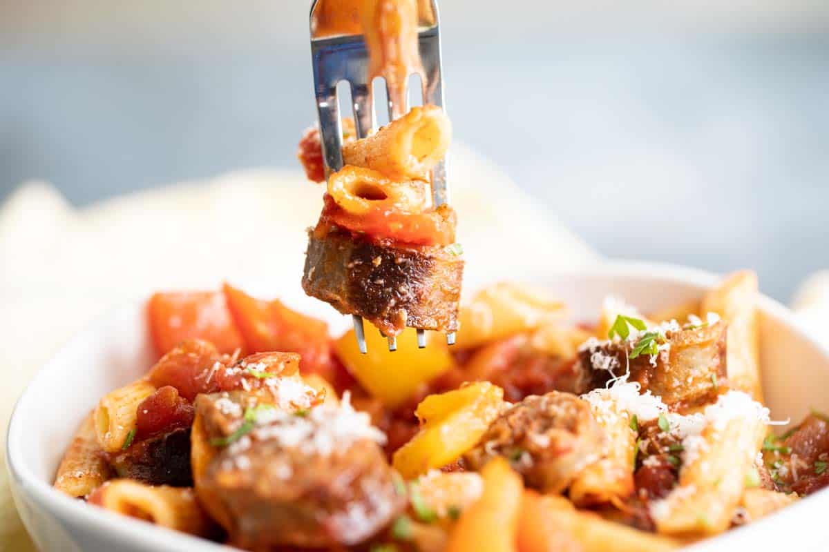 fork with a slice of sausage, a pepper and penne pasta