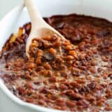 Baked beans with bacon in a casserole dish with a wooden spoon to scoop