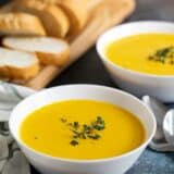 bowls of butternut squash soup with bread in the background