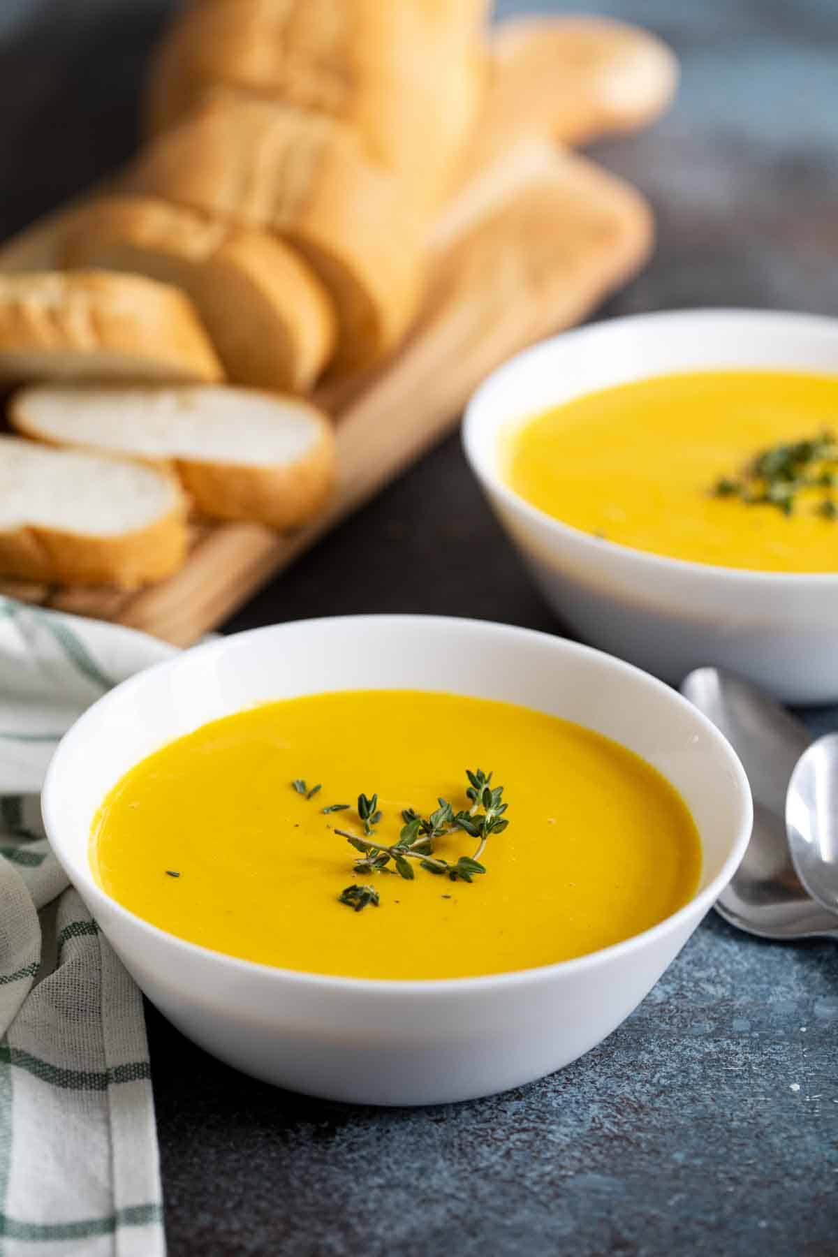 bowls of butternut squash soup with bread in the background