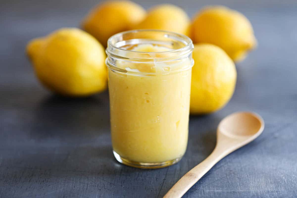jar of lemon curd with a wooden spoon and lemons in the background