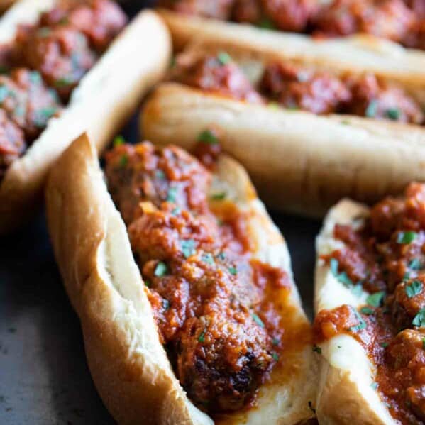 several meatball subs on a tray topped with marinara and parsley