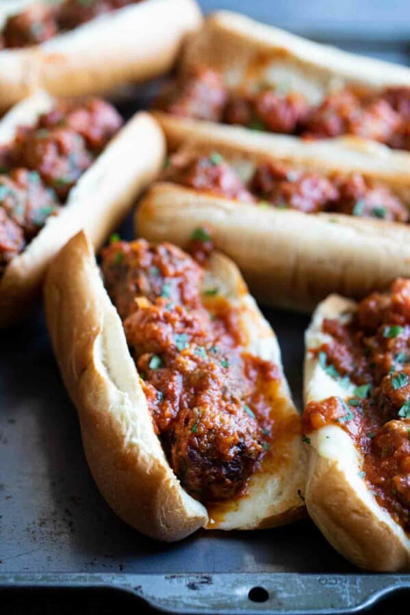 several meatball subs on a tray topped with marinara and parsley