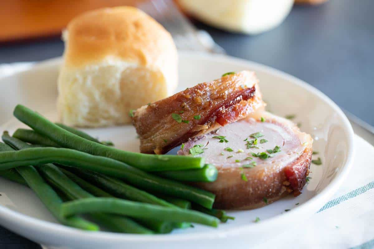 plate with slices of bacon wrapped pork tenderloin and green beans