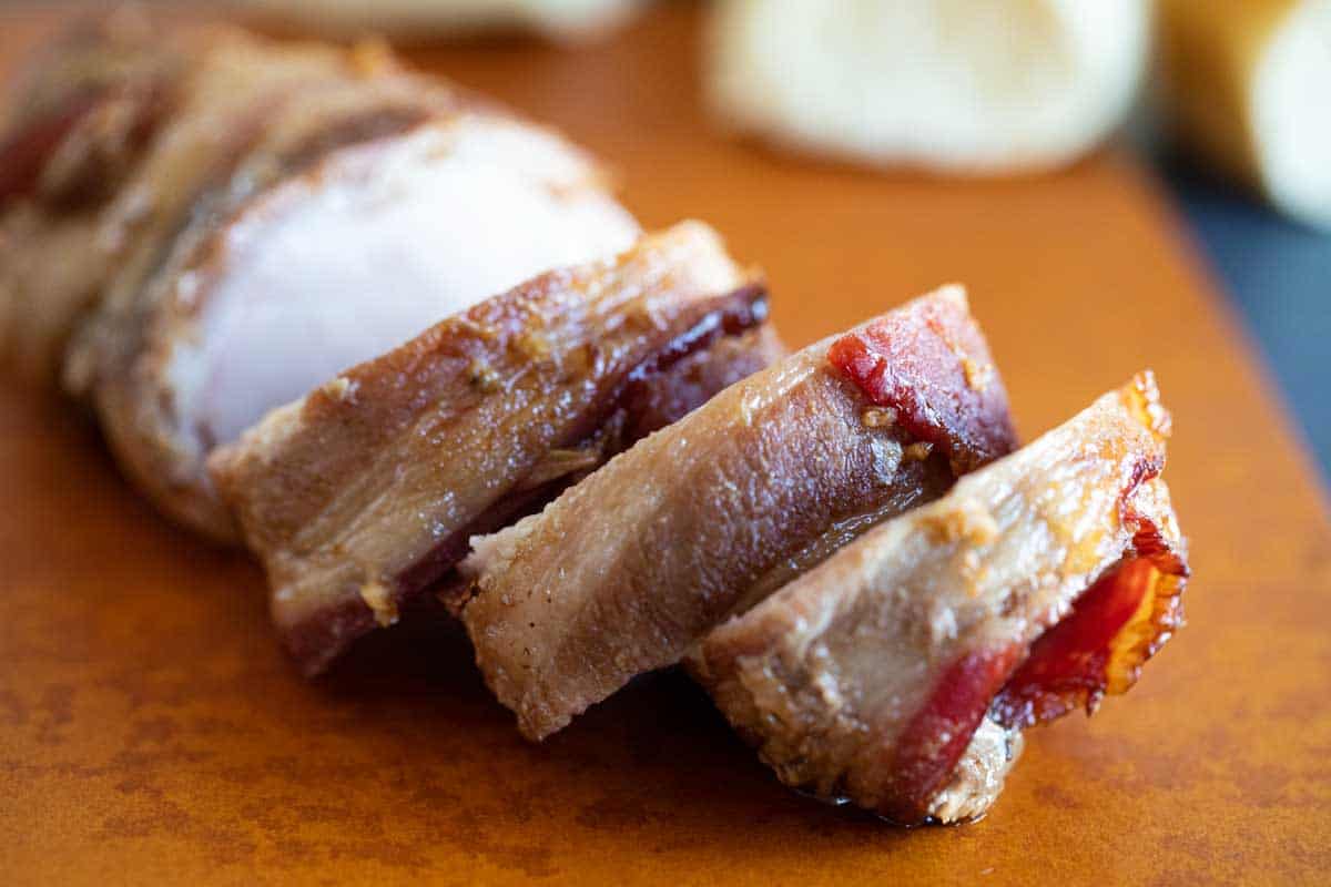 sliced bacon wrapped pork tenderloin on a cutting board