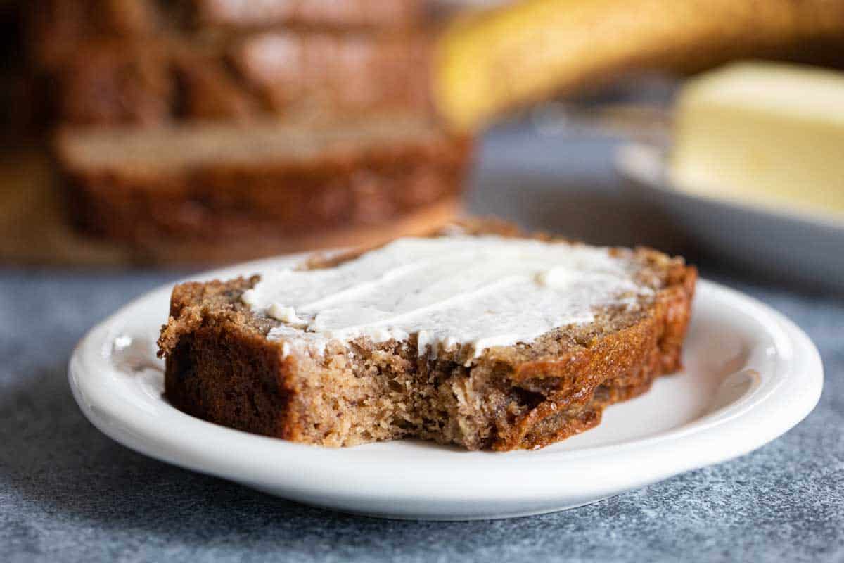 slice of banana bread with butter on a plate with a bite taken from it