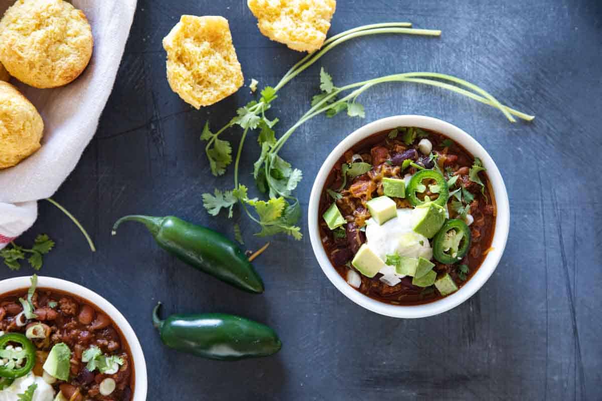 overhead view of bowl of crock pot chili with toppings and a corn muffin on the side