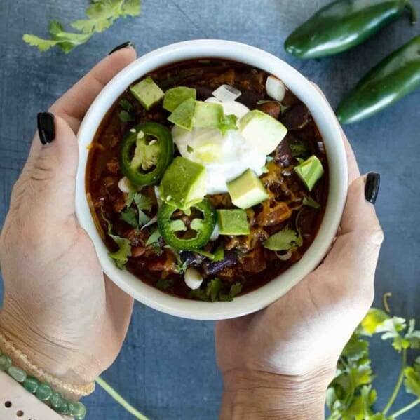 overhead view of two hands holding a bowl of chili