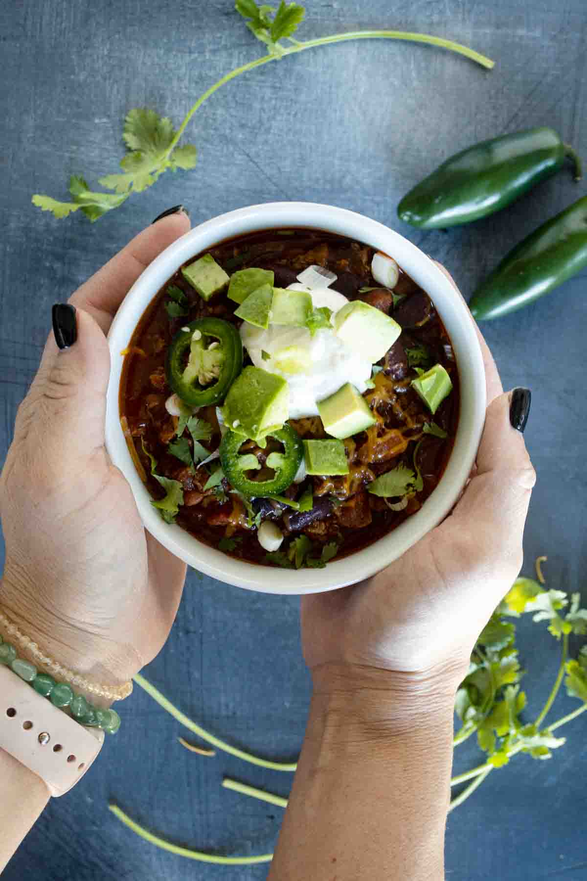 overhead view of two hands holding a bowl of chili