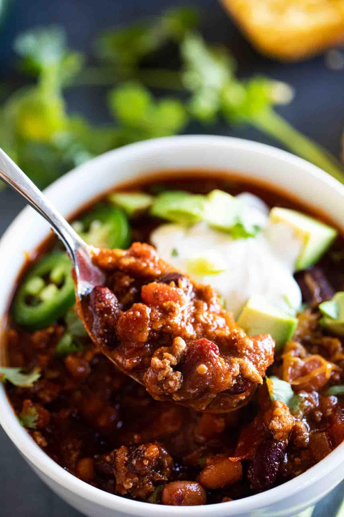 spoon full of chili topped with sour cream and avocados