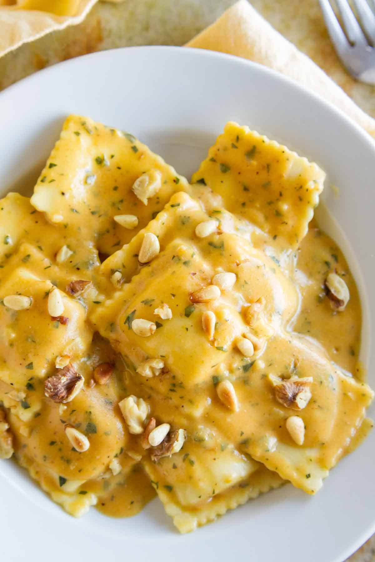 overhead view of ravioli with pumpkin pasta sauce topped with pine nuts and walnuts