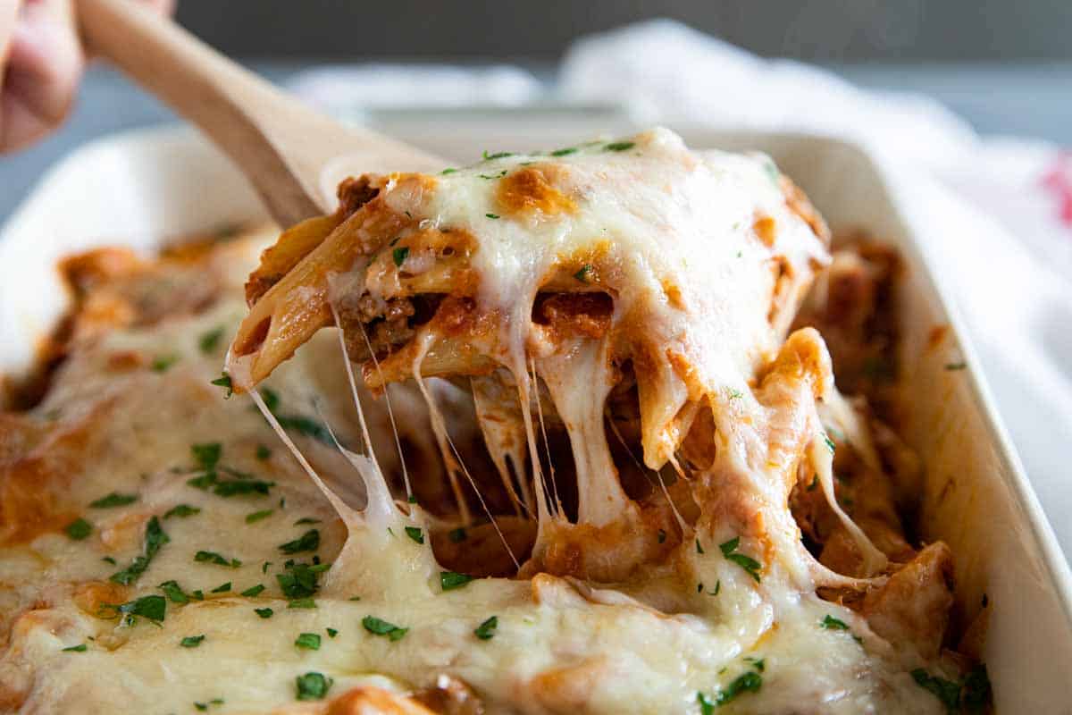 taking a scoop of penne pasta bake out of casserole dish