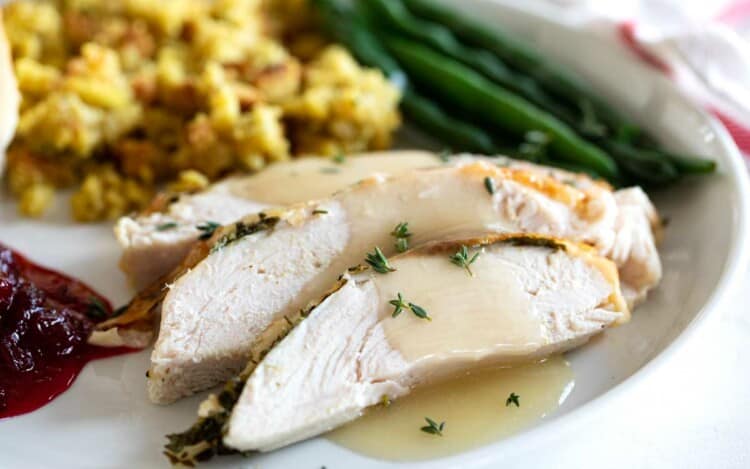 slices of roast turkey breast with gravy and side dishes on a plate