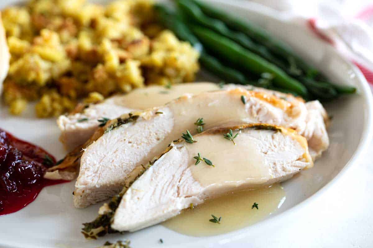 slices of roast turkey breast with gravy and side dishes on a plate