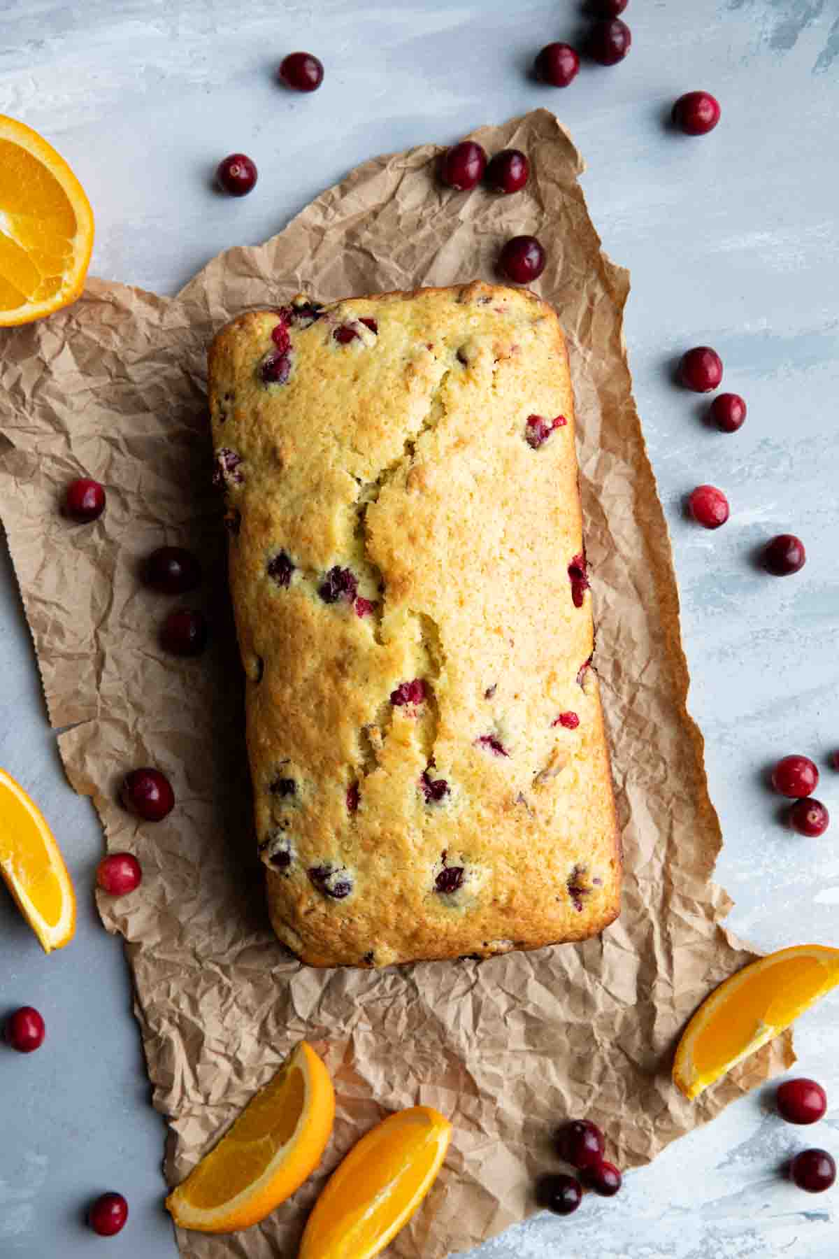 full loaf of cranberry orange bread surrounded by fresh cranberries and orange slices