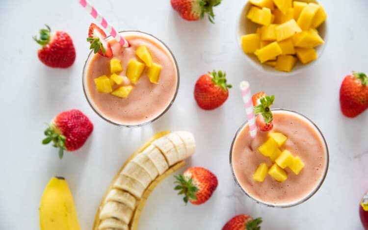 overhead view of tropical smoothie with fruit around the cups