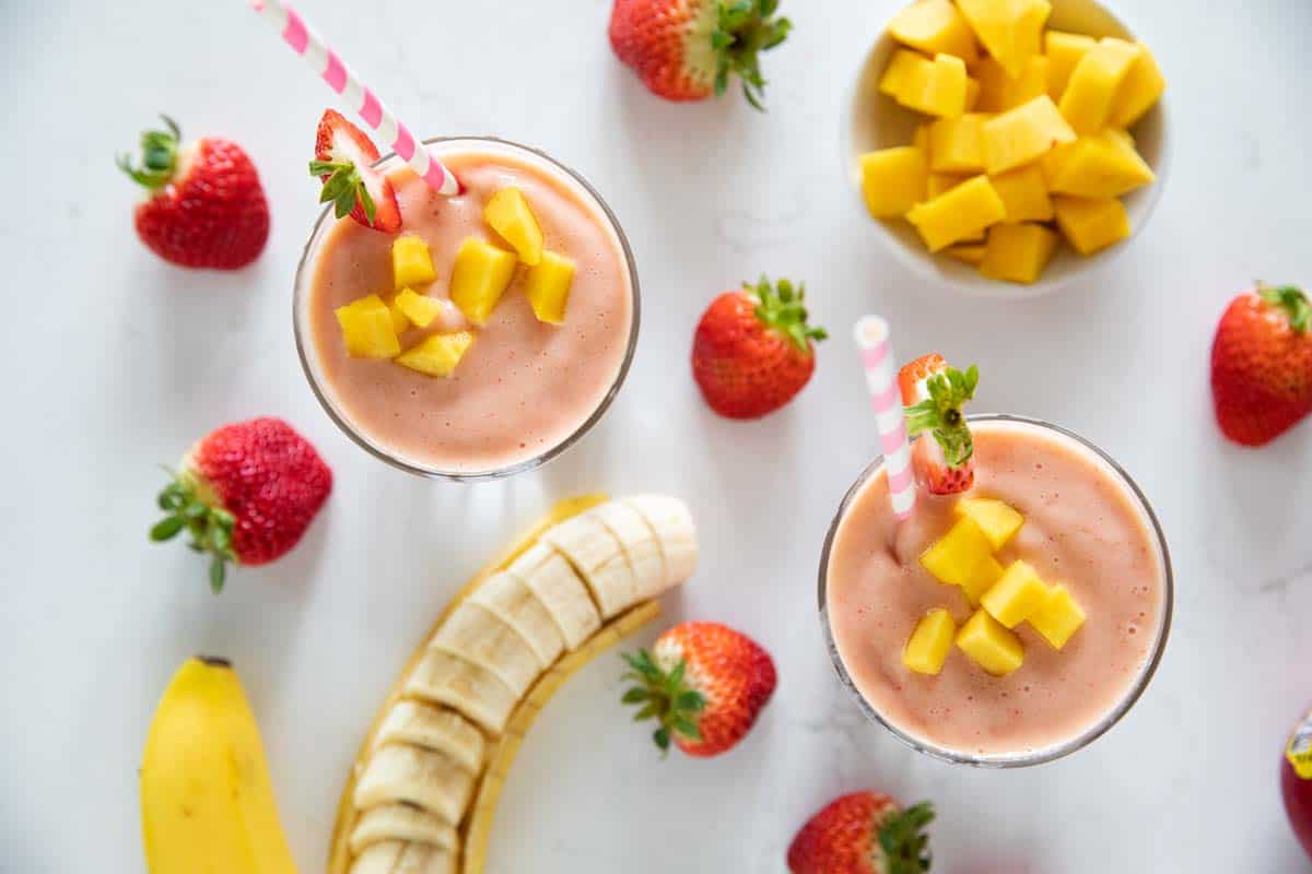 overhead view of tropical smoothie with fruit around the cups