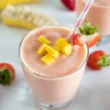 cup of tropical smoothie with a straw topped with mango and strawberry