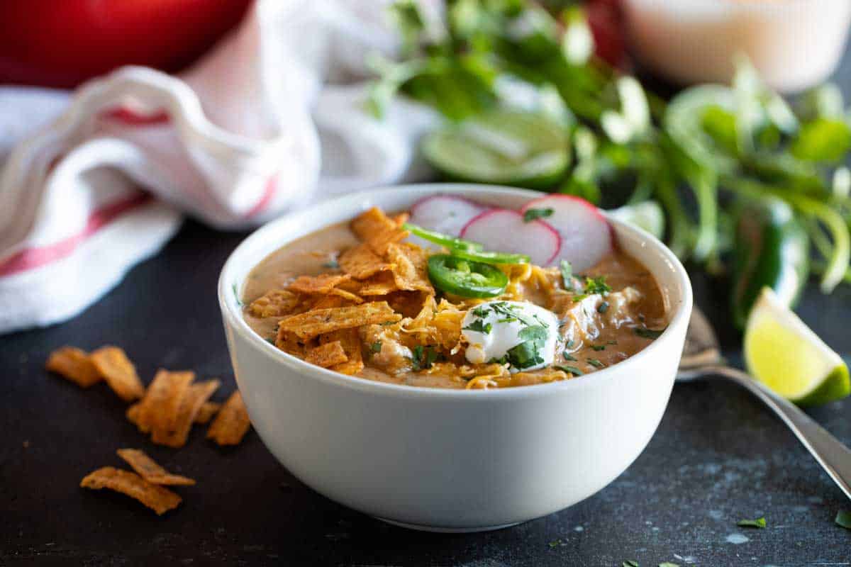 bowl of chicken enchilada soup topped with sour cream, tortilla strips, and jalapeno