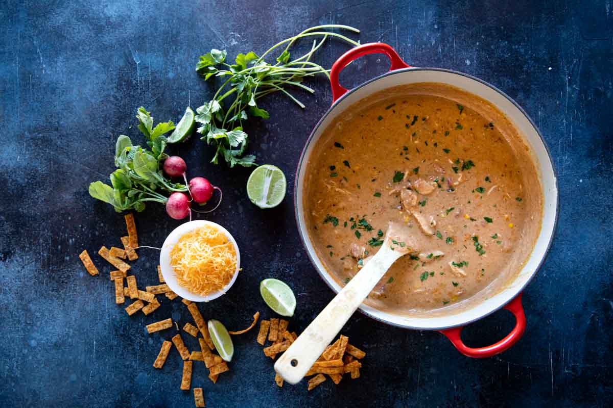 overhead view of pot of chicken enchilada soup and toppings on the side