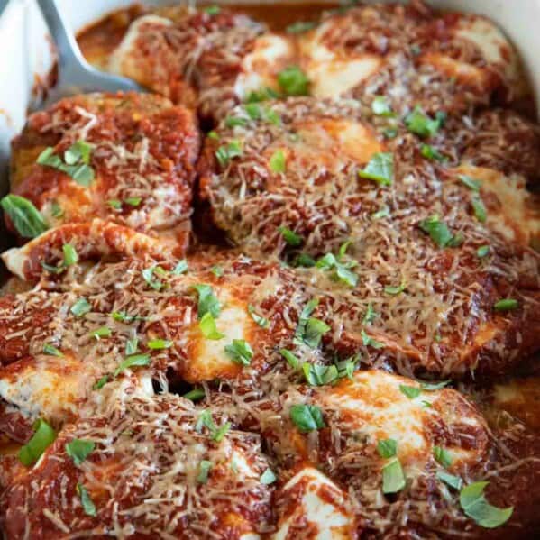 white casserole dish with eggplant parmesan with spatula.