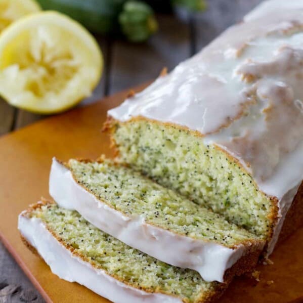 loaf of lemon poppy seed zucchini bread on a cutting board with the first slices cut.