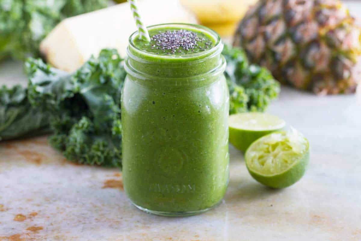 Kale Smoothie topped with chia seeds with fruit and kale in the background