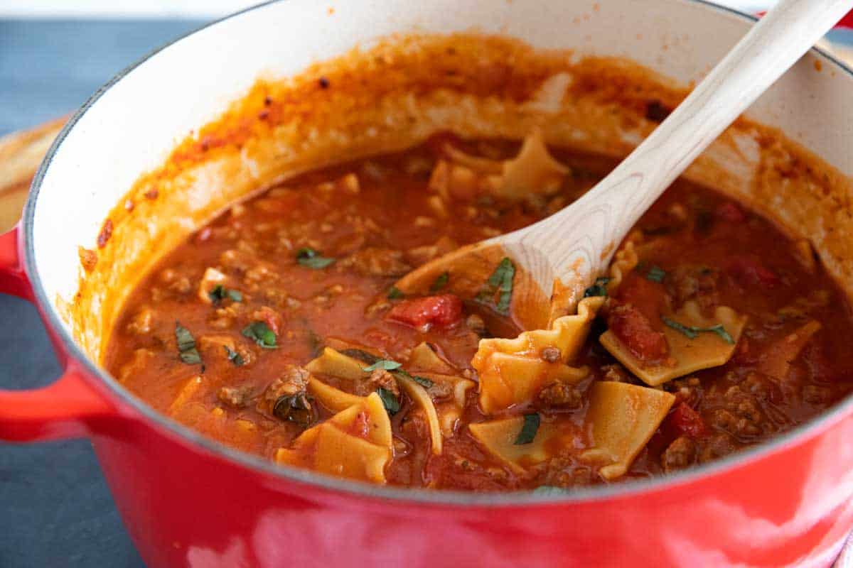 red dutch oven filled with lasagna soup with a wooden ladle