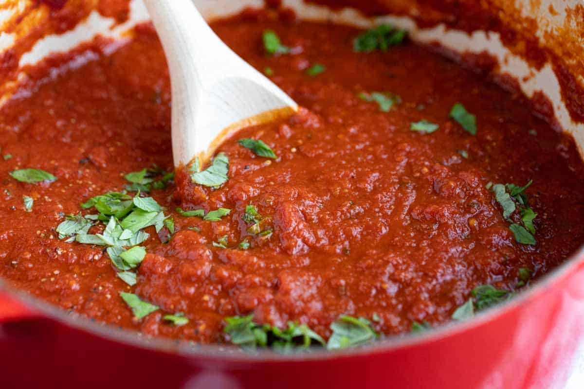 pot with homemade marinara sauce with fresh basil sprinkled on top.