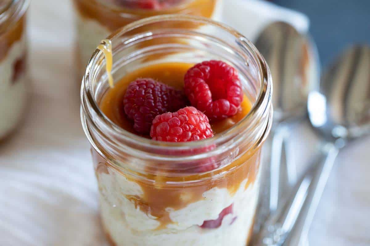 Jar with rice pudding topped with salted caramel and raspberries.