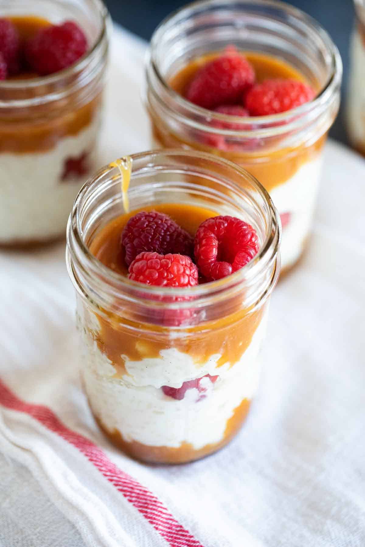 jars filled with rice pudding with caramel and fresh raspberries.