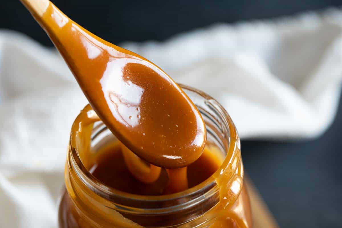 Homemade salted caramel sauce dripping from a spoon in a jar of sauce.
