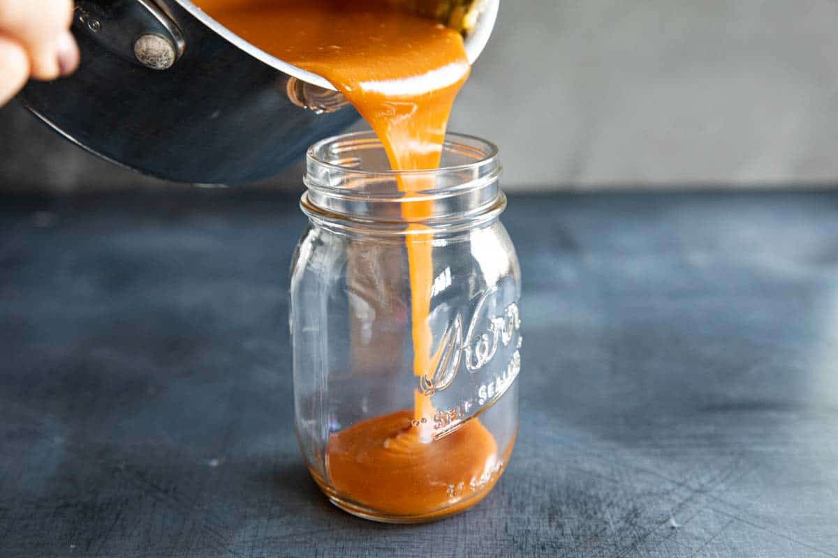 pouring hot caramel into a jar from a saucepan.