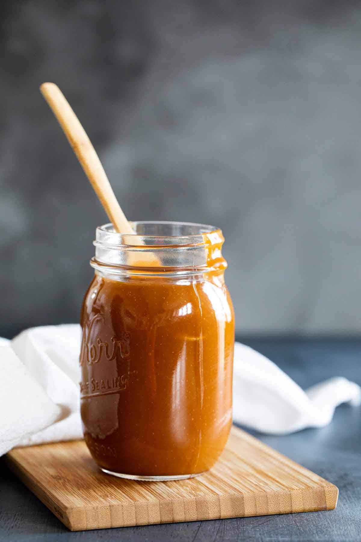 homemade caramel sauce in a jar sitting on a wooden board.