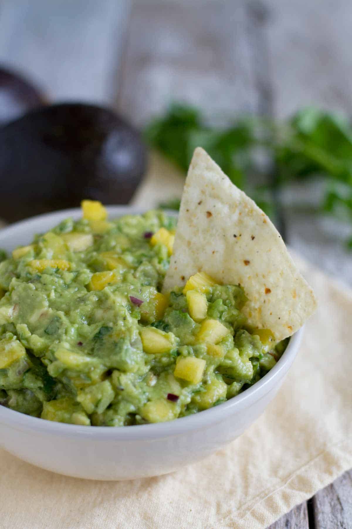 Bowl filled with Tropical Guacamole with a tortilla chip.