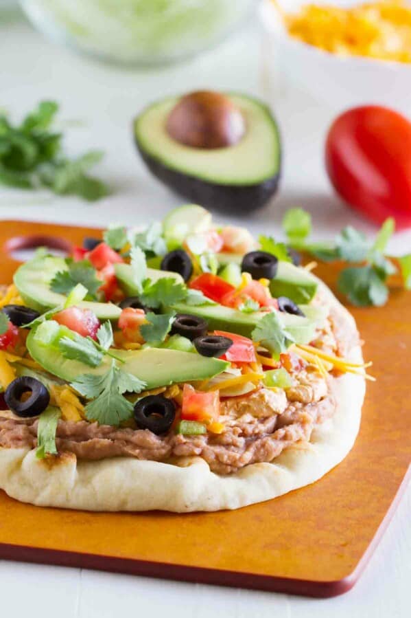 7 layer flatbread on a cutting board with ingredients in the background