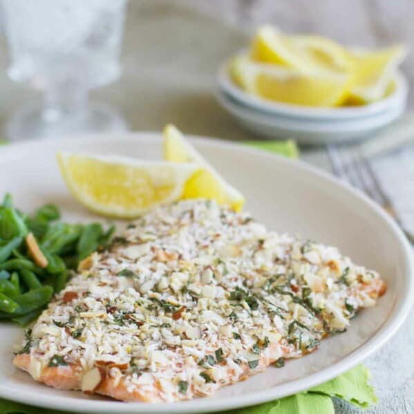 salmon fillet coated with almonds and herbs on a plate with lemon slices