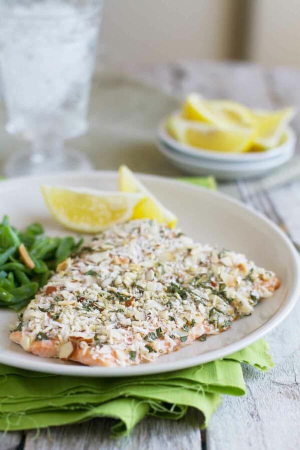 salmon fillet coated with almonds and herbs on a plate with lemon slices