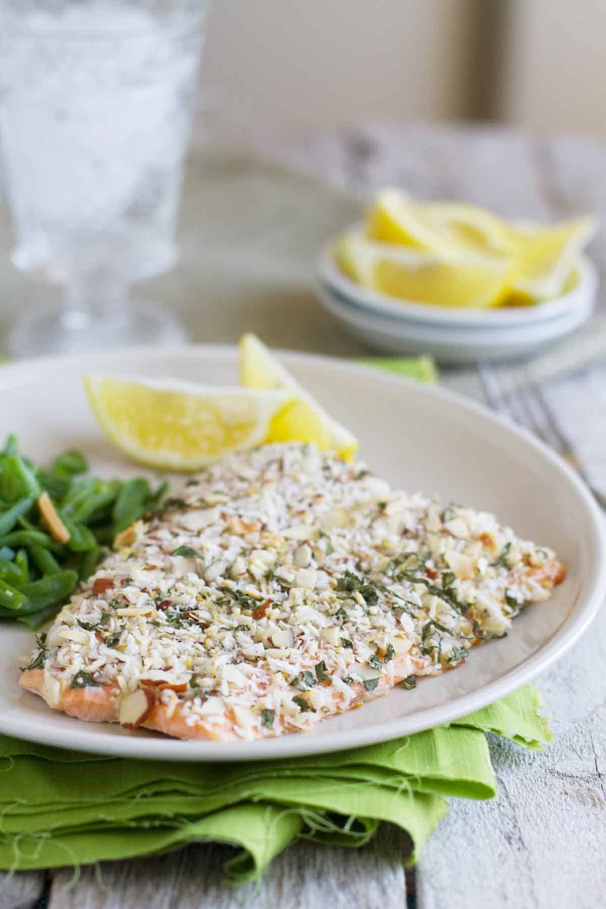 Salmon is topped with an almond and breadcrumb topping in this easy and quick Almond Crusted Salmon. salmon fillet coated with almonds and herbs on a plate with lemon slices