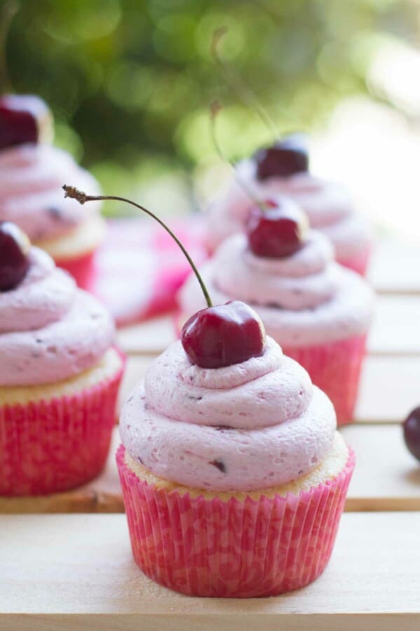 Almond cupcakes topped with fresh cherry frosting with a fresh cherry on top