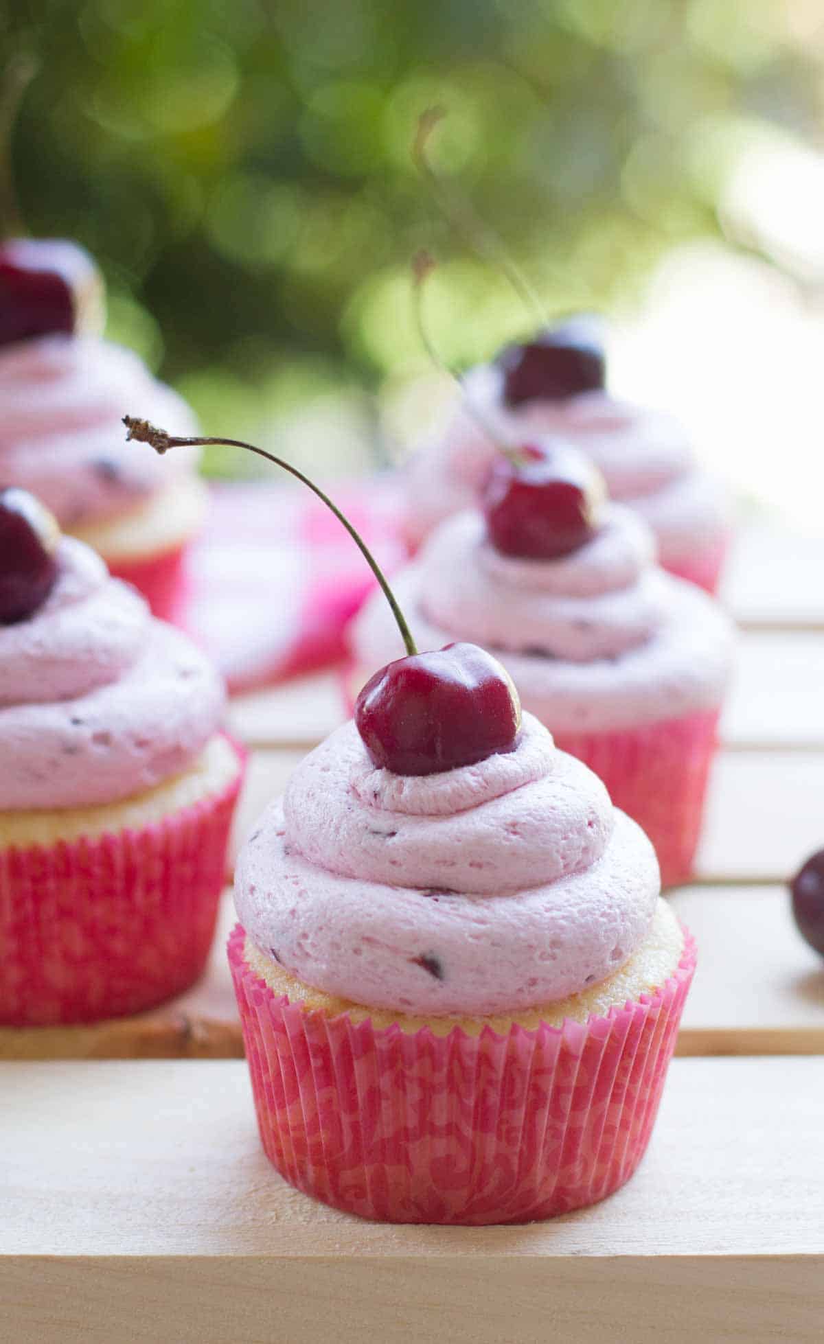 Almond cupcakes topped with fresh cherry frosting with a fresh cherry on top