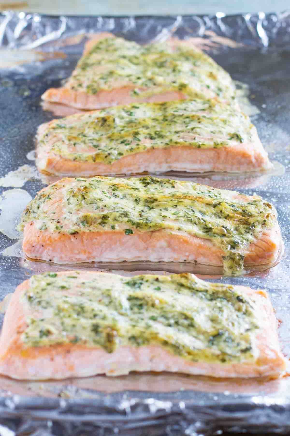 4 pieces of salmon on a baking sheet topped with mayonnaise and herb topping