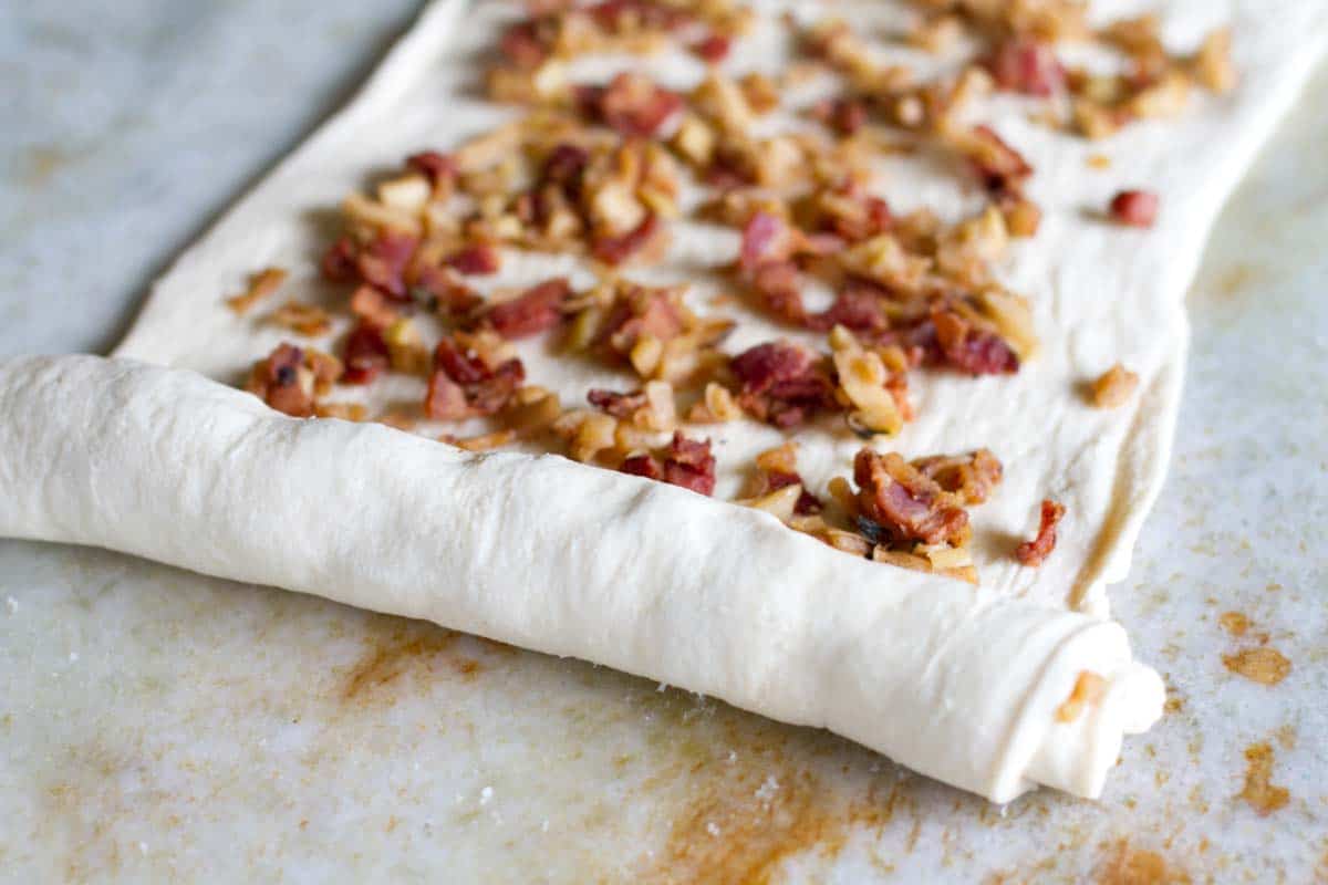 rolling up dough over apple and bacon filling
