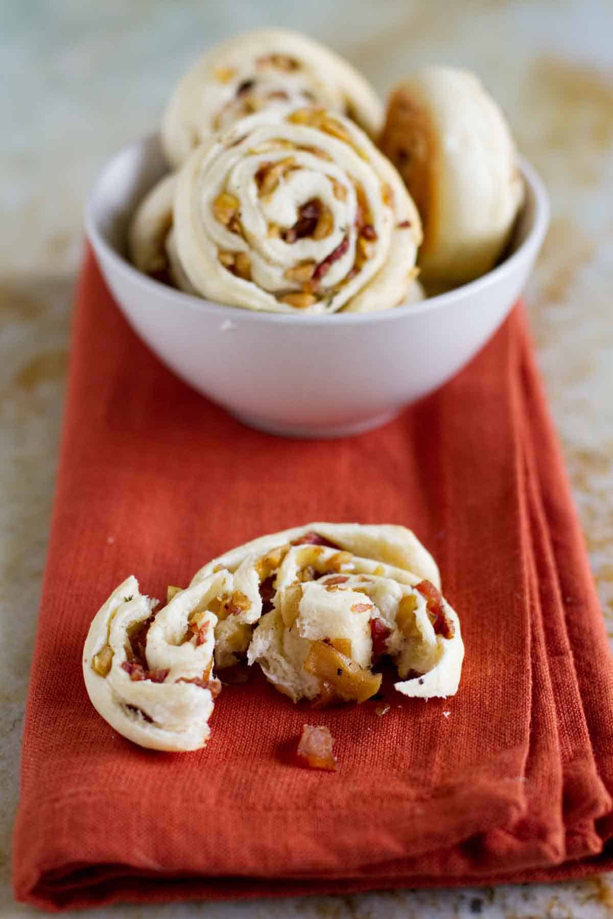 apple bacon pinwheel torn apart to show texture with bowl of more pinwheels behind
