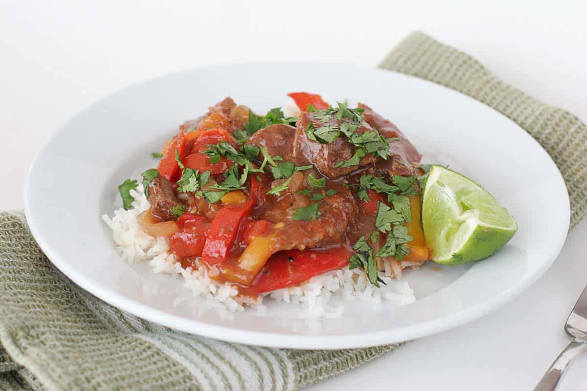 Asian Pepper Steak - sirloin is cooked in the slow cooker with peppers, ginger, and garlic, and served over rice for a delicious slow cooked meal. Asian Pepper Steak on a plate with a lime wedge