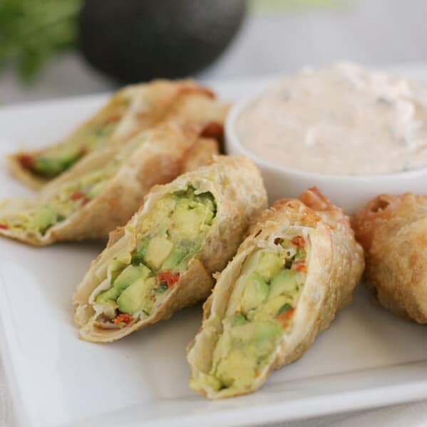 Avocado Egg Rolls cut in half on a plate with a bowl of chipotle ranch dipping sauce